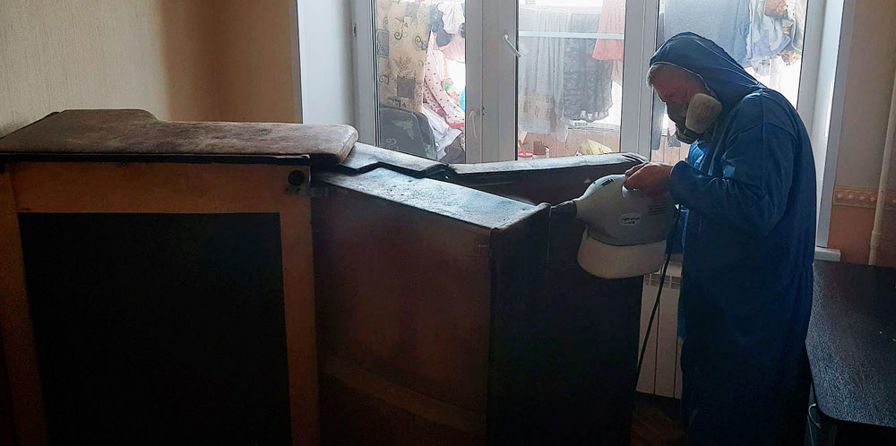 Дезинфектор проливает инсектицидным препаратом поверхности зараженного дивана.